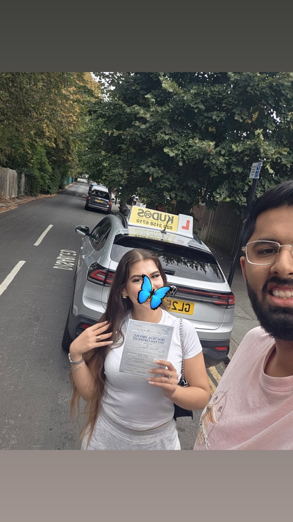 A learner holding her practical driving test pass certificate next to her instructor